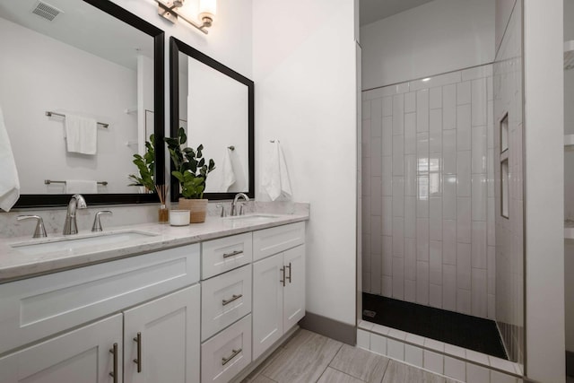 full bath featuring double vanity, tiled shower, a sink, and visible vents