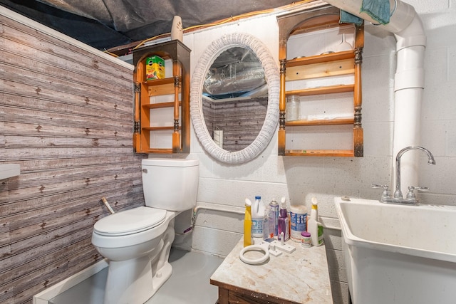 bathroom with a sink, toilet, and concrete block wall