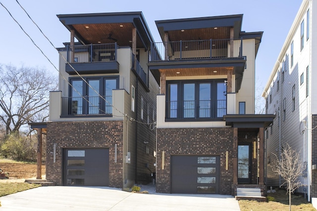 contemporary home with an attached garage, a balcony, concrete driveway, and brick siding