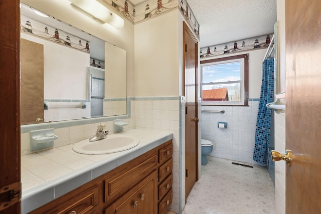 full bath featuring a textured ceiling, toilet, vanity, visible vents, and wainscoting