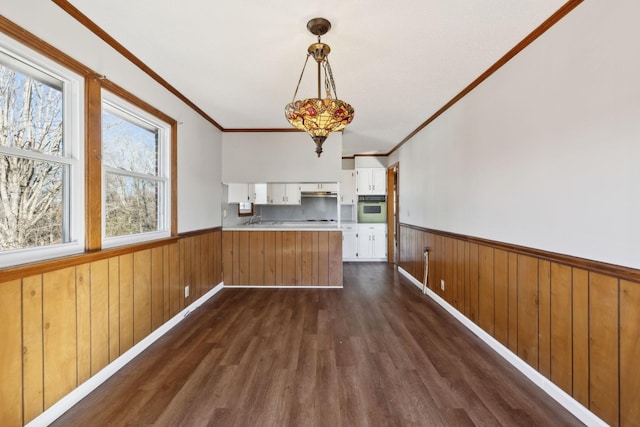 kitchen with white oven, wainscoting, white cabinetry, wooden walls, and a peninsula