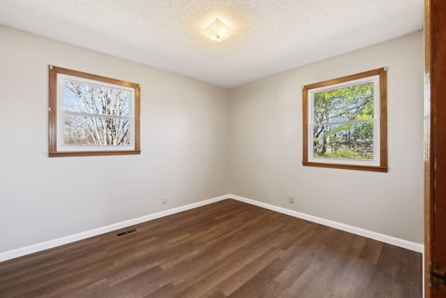 unfurnished room featuring baseboards, visible vents, dark wood finished floors, and a textured ceiling