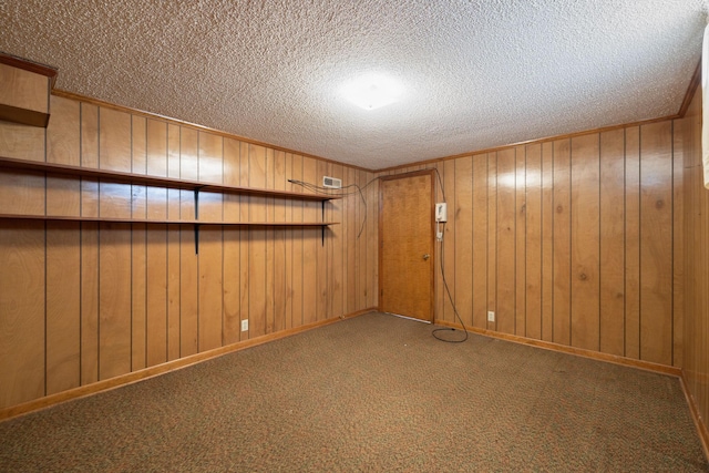 empty room with a textured ceiling, wooden walls, carpet floors, visible vents, and baseboards