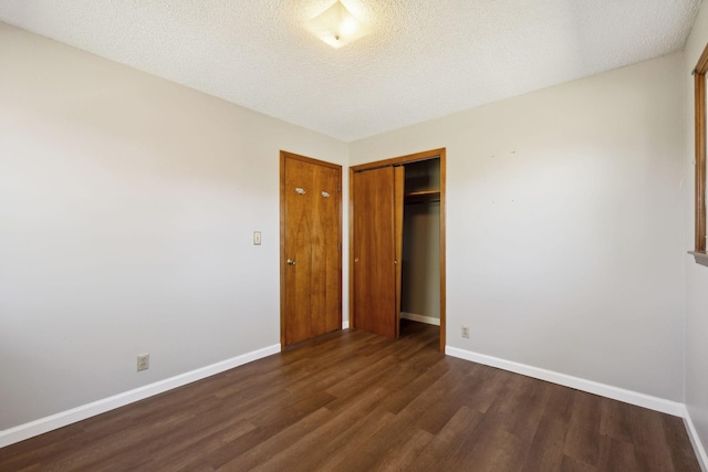 unfurnished bedroom with a textured ceiling, baseboards, dark wood-style flooring, and a closet