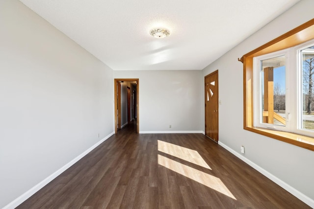 spare room featuring dark wood-style flooring and baseboards