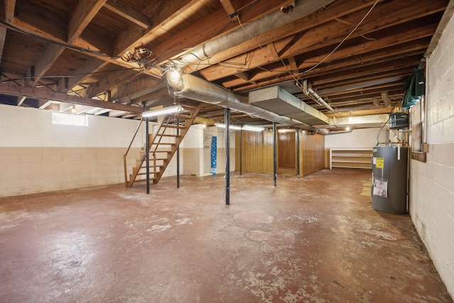 below grade area featuring concrete block wall, electric water heater, and stairs