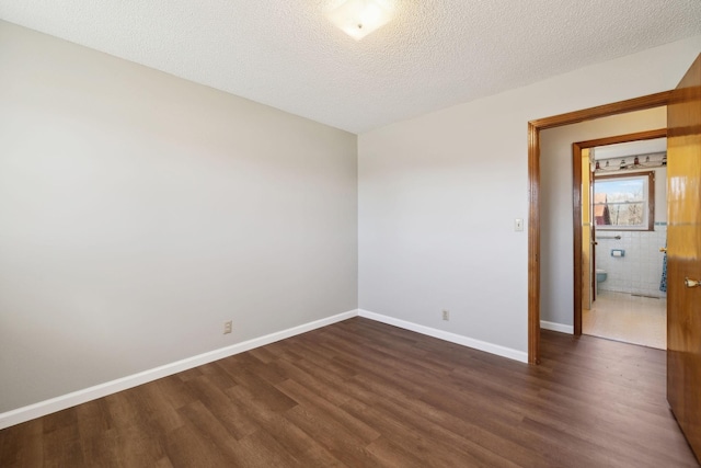 unfurnished room featuring dark wood-style floors, baseboards, and a textured ceiling