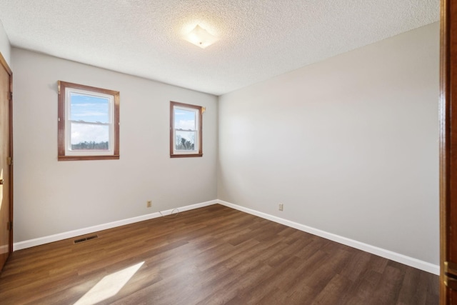 empty room with dark wood-style floors, visible vents, a textured ceiling, and baseboards