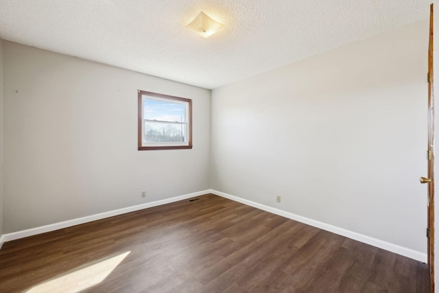 unfurnished room with a textured ceiling, dark wood-style flooring, and baseboards