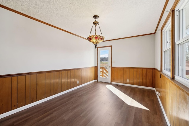 empty room featuring wooden walls, a wainscoted wall, wood finished floors, crown molding, and a textured ceiling