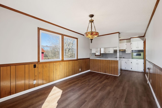 kitchen featuring dark wood-style floors, white oven, a wainscoted wall, white cabinets, and a peninsula