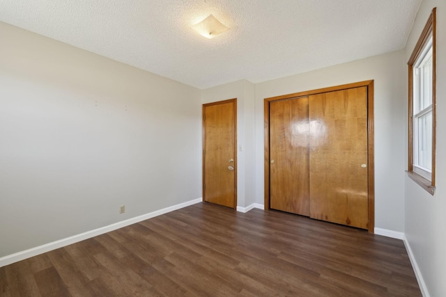 unfurnished bedroom with a closet, dark wood finished floors, a textured ceiling, and baseboards