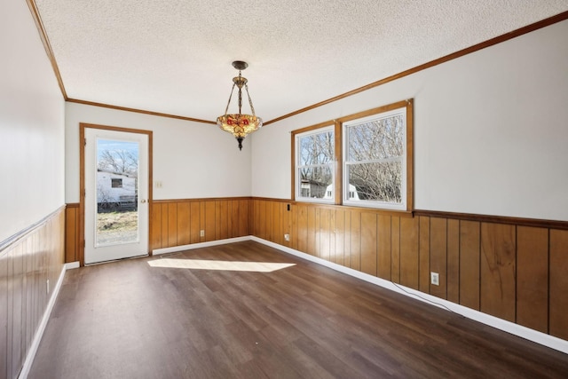 spare room with a textured ceiling, wooden walls, ornamental molding, wainscoting, and dark wood-style floors