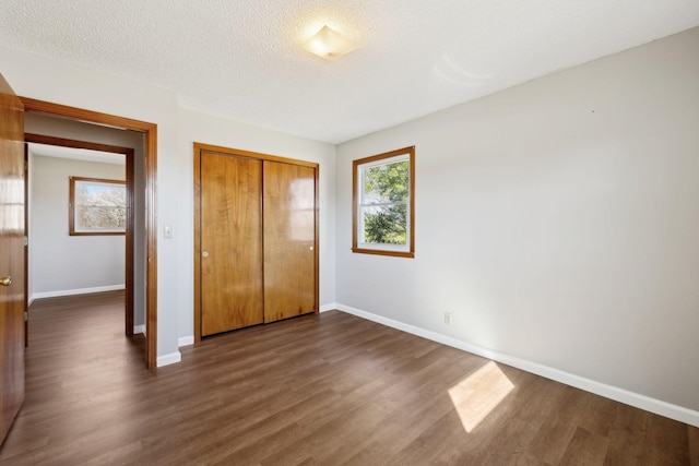 unfurnished bedroom with a textured ceiling, baseboards, dark wood finished floors, and a closet