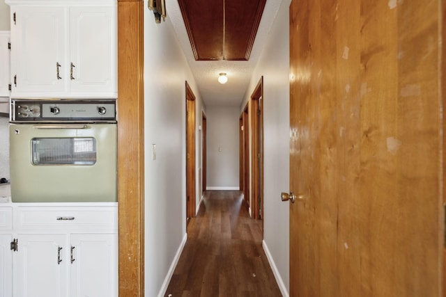 hall with attic access, a textured ceiling, baseboards, and dark wood-type flooring