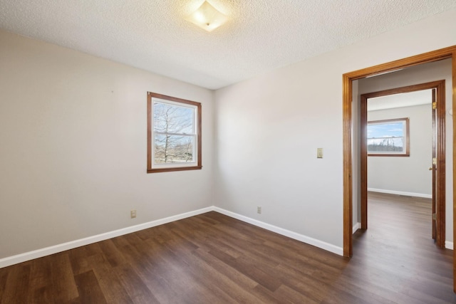 empty room featuring a textured ceiling, dark wood-type flooring, and baseboards