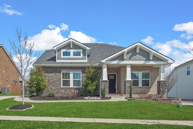 craftsman-style house featuring a front yard, cooling unit, stone siding, and roof with shingles