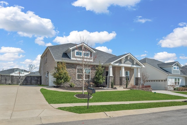 craftsman-style home with a front yard, fence, an attached garage, concrete driveway, and stone siding