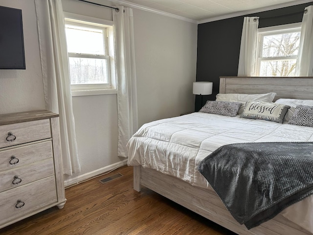 bedroom featuring baseboards, visible vents, crown molding, and wood finished floors