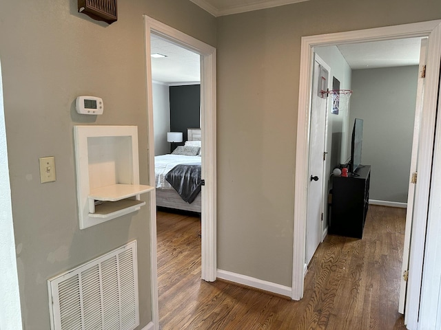 hall featuring visible vents, crown molding, baseboards, and wood finished floors