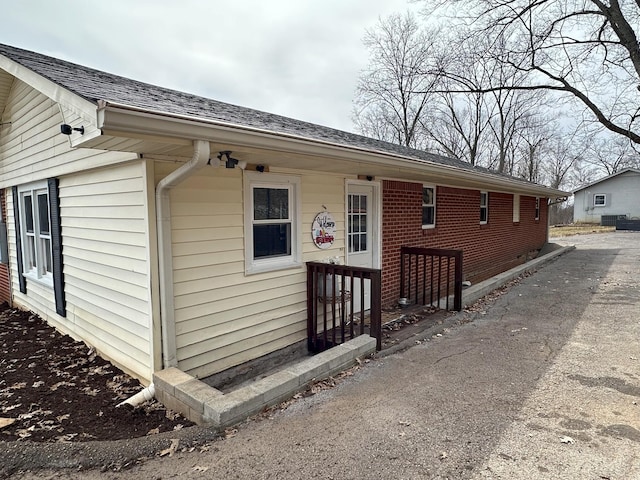 exterior space featuring roof with shingles and brick siding