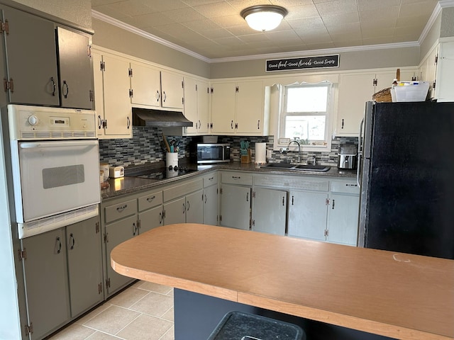 kitchen with white oven, freestanding refrigerator, a sink, under cabinet range hood, and black electric cooktop