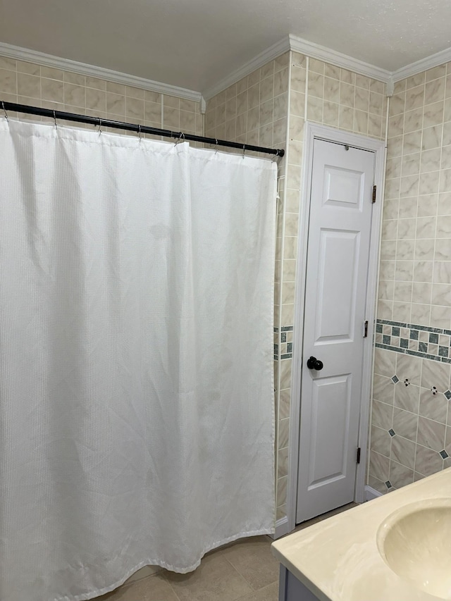 full bathroom featuring ornamental molding, tile patterned flooring, a sink, and tile walls