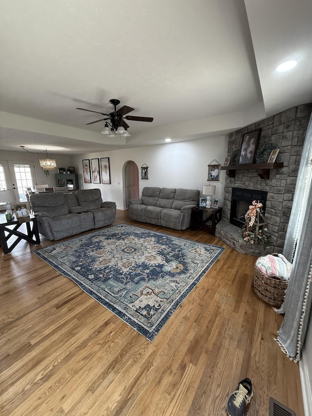 living area with visible vents, arched walkways, wood finished floors, a fireplace, and ceiling fan with notable chandelier