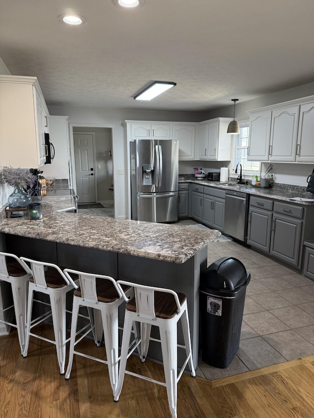 kitchen with stainless steel appliances, a peninsula, a sink, a kitchen breakfast bar, and gray cabinets