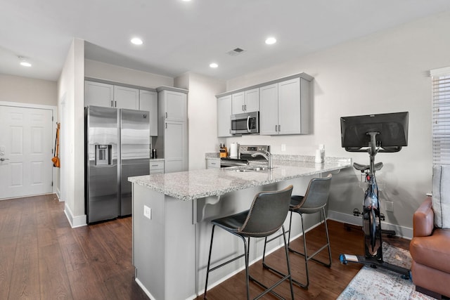 kitchen with light stone counters, a peninsula, dark wood-style flooring, visible vents, and appliances with stainless steel finishes