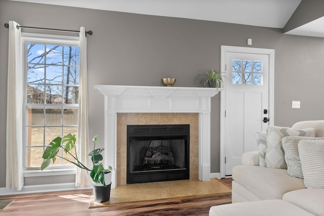 living room featuring a tile fireplace, a healthy amount of sunlight, visible vents, and wood finished floors