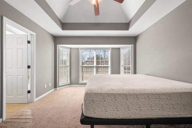 bedroom with baseboards, a ceiling fan, light colored carpet, lofted ceiling, and a tray ceiling