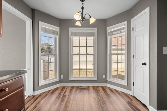 unfurnished dining area featuring a notable chandelier, dark wood-type flooring, visible vents, and baseboards