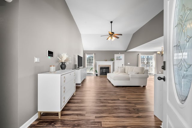 living area with dark wood-type flooring, plenty of natural light, a fireplace, and ceiling fan with notable chandelier