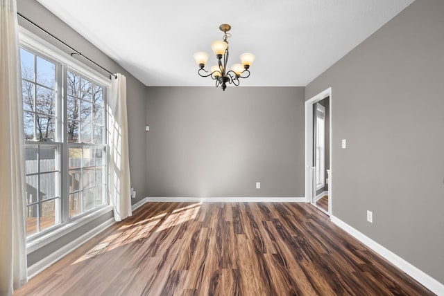 empty room with a chandelier, baseboards, and wood finished floors