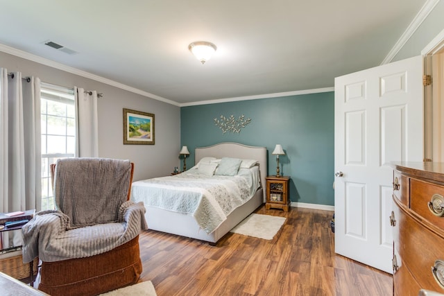 bedroom with ornamental molding, wood finished floors, visible vents, and baseboards