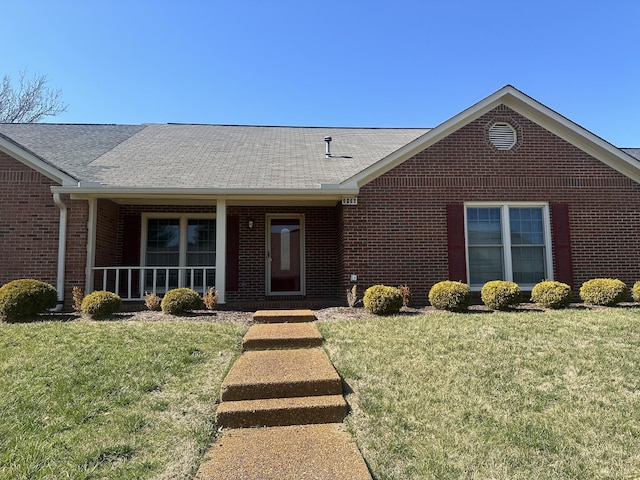 ranch-style house with covered porch, a shingled roof, a front lawn, and brick siding