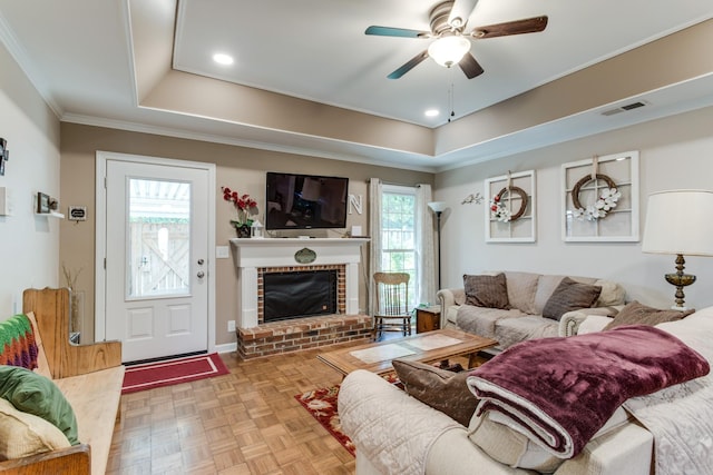 living area featuring ceiling fan, visible vents, a raised ceiling, and ornamental molding