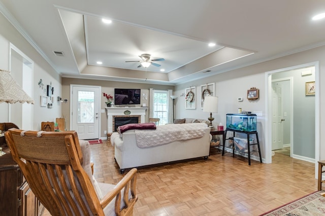 living room featuring a tray ceiling, crown molding, a fireplace, visible vents, and baseboards