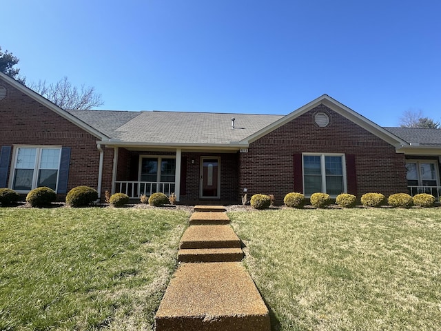 ranch-style home with a shingled roof, a front yard, and brick siding