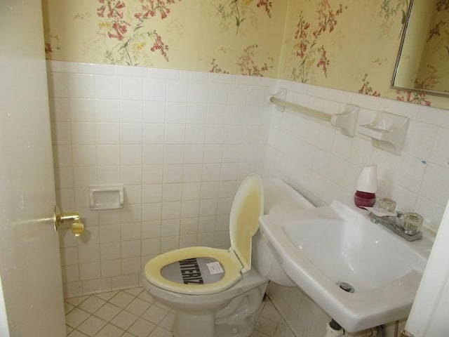 half bath featuring tile patterned flooring, wainscoting, a sink, and wallpapered walls