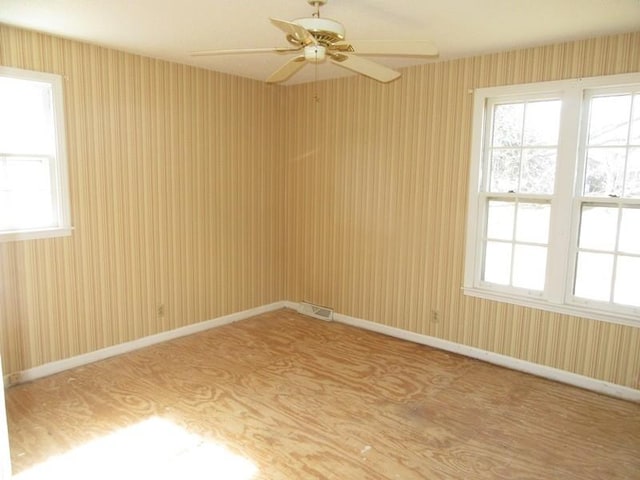 unfurnished room featuring wallpapered walls, baseboards, visible vents, and a ceiling fan