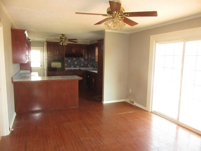 kitchen with a peninsula, ornamental molding, dark wood finished floors, and black oven