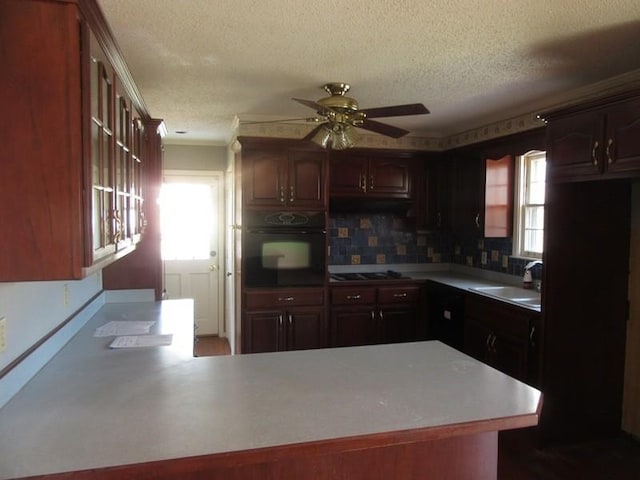 kitchen featuring glass insert cabinets, a peninsula, light countertops, black appliances, and a sink