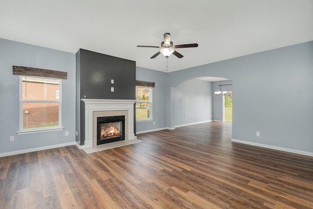 unfurnished living room with dark wood-style flooring, a high end fireplace, plenty of natural light, baseboards, and ceiling fan with notable chandelier