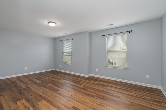 spare room featuring dark wood-type flooring, visible vents, and baseboards