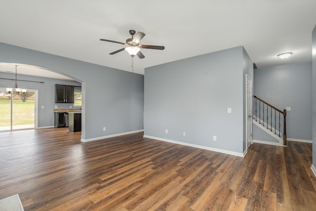 unfurnished living room featuring ceiling fan with notable chandelier, dark wood finished floors, baseboards, and stairs