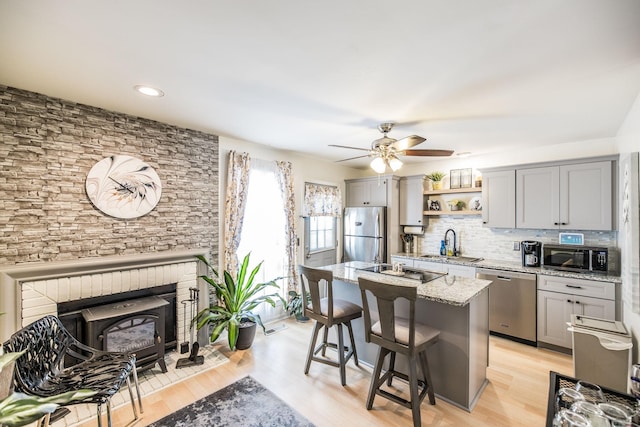 kitchen with a breakfast bar, a sink, appliances with stainless steel finishes, gray cabinets, and open shelves