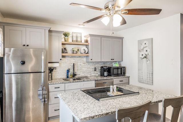 kitchen featuring light stone counters, gray cabinetry, a sink, appliances with stainless steel finishes, and tasteful backsplash