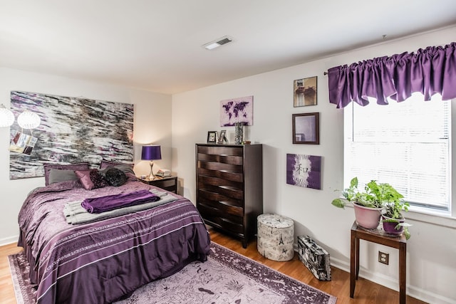 bedroom with baseboards, visible vents, and wood finished floors